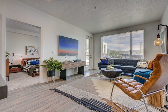 Modern living room with a cozy atmosphere, featuring a stylish seating area, large windows for natural light, and an adjacent bedroom view.