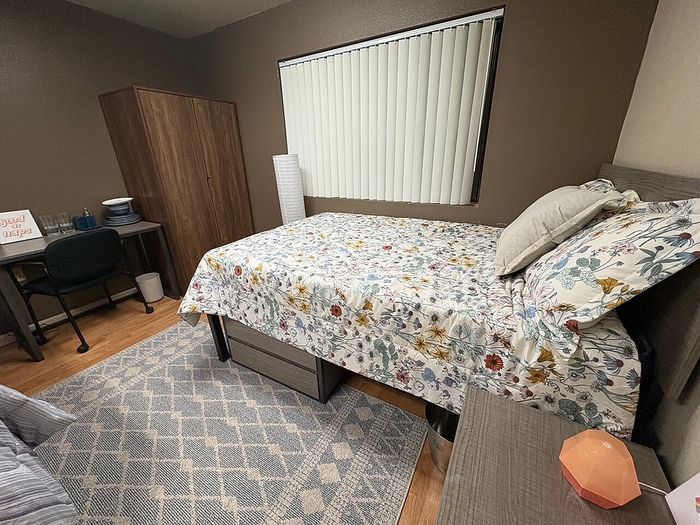 Cozy bedroom featuring a floral-patterned bedspread, elegant wooden wardrobe, and a functional workspace with a desk under soft, ambient lighting.