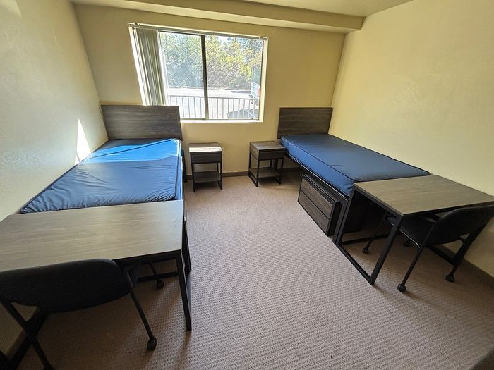 Bright and cozy room featuring two twin beds, study desks, and a large window with serene outdoor views.
