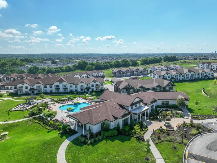 Scenic aerial view of luxury apartment complex featuring stylish buildings, lush green landscaping, and a sparkling swimming pool.