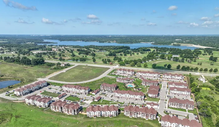 Scenic aerial view of a tranquil apartment complex surrounded by lush greenery and a picturesque lake, ideal for serene living.