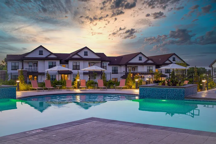 Luxurious apartment complex with a sparkling pool, elegant loungers, and ambient evening lighting under a stunning sunset sky.