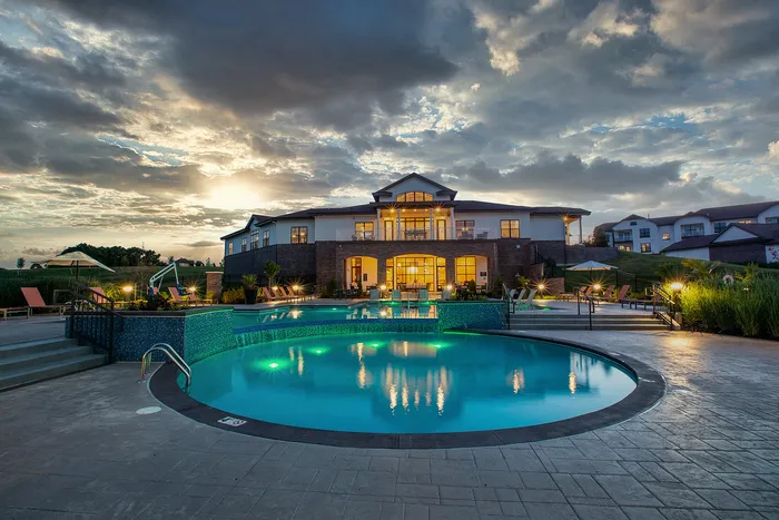 Luxurious apartment building with an inviting illuminated pool at sunset, surrounded by lush greenery and modern lounge chairs.