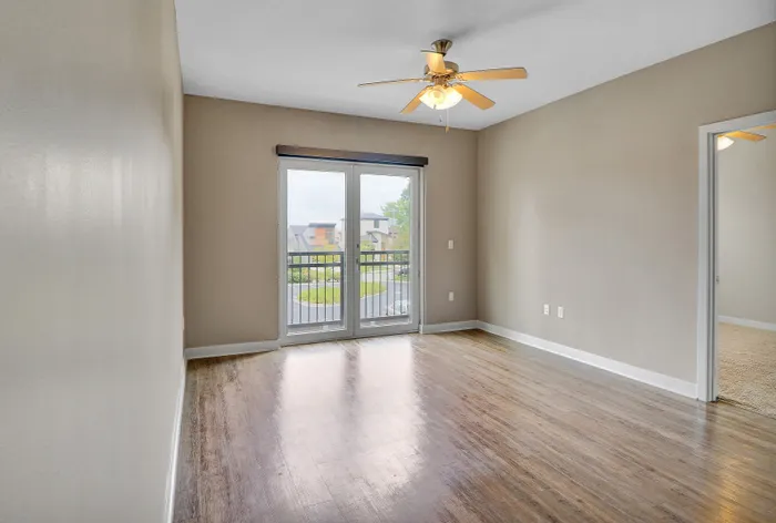 Bright, airy apartment with elegant wood flooring and a private balcony view, complemented by a modern ceiling fan.