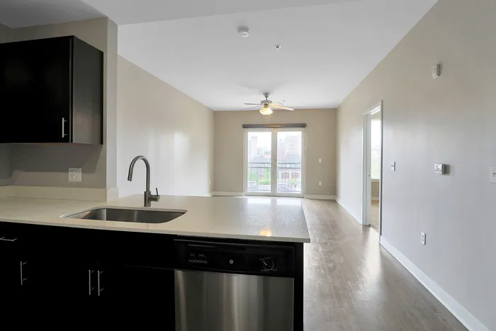Modern open-plan apartment with a sleek kitchen island, hardwood floors, and a bright living space leading to a balcony with city views.