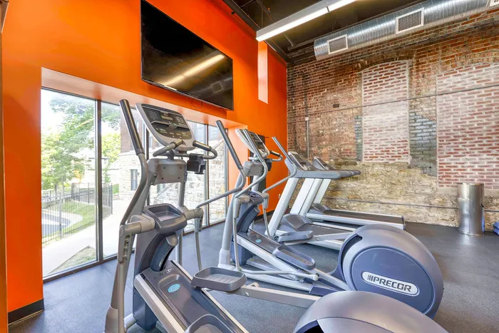 Modern fitness center with state-of-the-art exercise machines, vibrant orange walls, and rustic exposed brick accent.