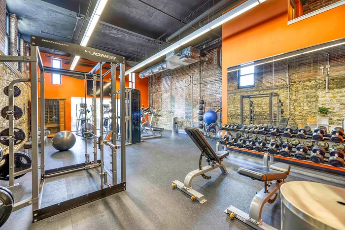 Modern fitness center featuring state-of-the-art weightlifting equipment, vibrant orange accents, and exposed brick walls for an industrial chic look.