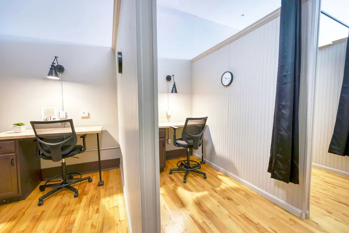 Modern workspace with two private desks, warm lighting, stylish decor, and elegant hardwood flooring.