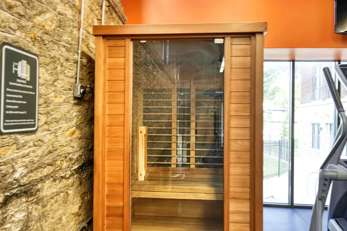 Charming wooden sauna room with a glass door, set against a rustic stone wall, offering a cozy and relaxing oasis.