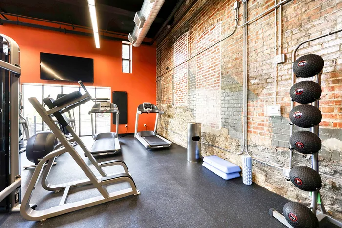 Modern gym with exposed brick walls, featuring treadmills and a rack of medicine balls in a vibrant workout space.