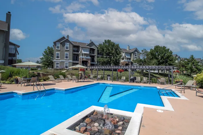 Inviting apartment complex with stunning pool, comfortable lounging areas, and lush landscaping under a bright blue sky.