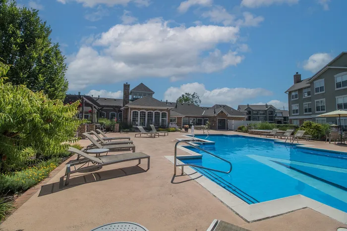 Luxurious apartment complex with a sparkling outdoor pool, surrounded by elegant loungers and lush landscaping under a bright blue sky.