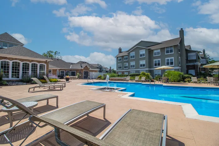 Luxurious apartment complex with a stunning outdoor pool, sun loungers, and landscaped surroundings under a clear blue sky.