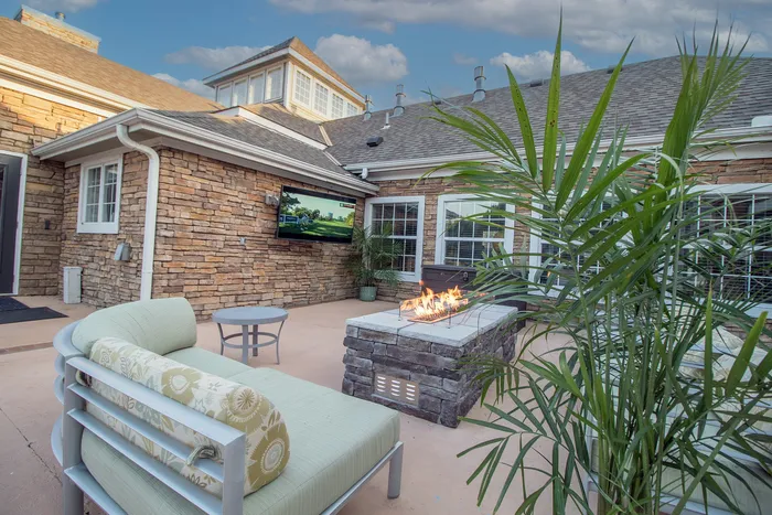 Charming outdoor patio with cozy seating, modern fire pit, and elegant stone facade, perfect for entertaining.