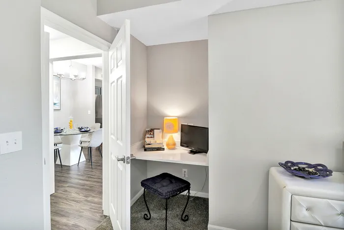 Chic apartment interior showcasing a cozy workspace with a sleek desk, modern lighting, and inviting view into a stylish dining area.
