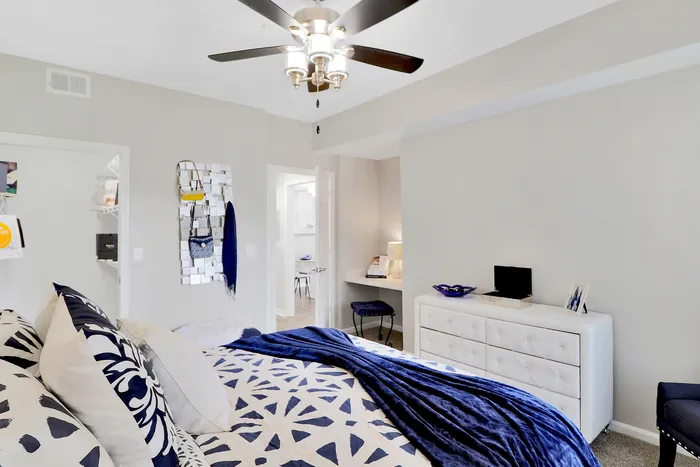Bright and stylish bedroom featuring elegant ceiling fan, plush bedding with blue accents, and chic modern decor.
