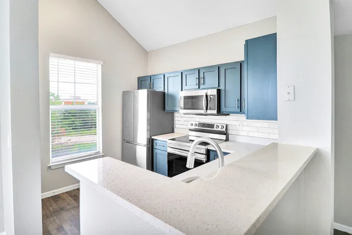 Chic kitchen with modern blue cabinetry, stainless steel appliances, and a bright window view.