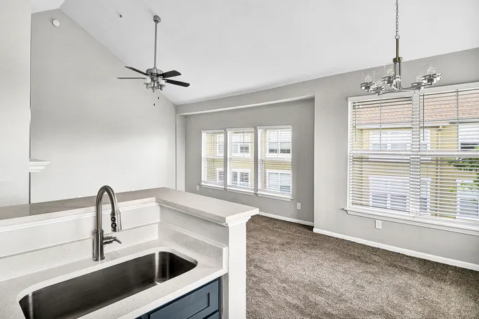 Bright and airy modern apartment interior showcasing an open-concept kitchen with sleek countertops and a cozy living area enhanced by large windows that invite natural light.