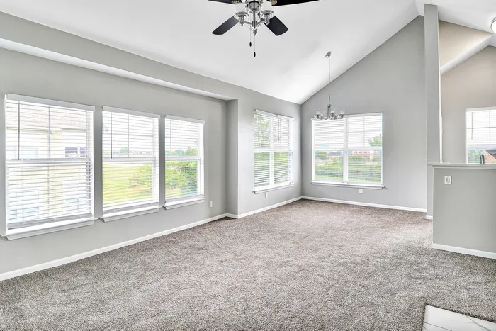 Bright and airy living room with vaulted ceiling, large windows, and elegant gray carpeting.