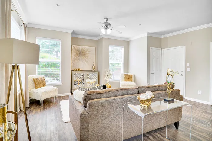 Inviting living room with modern decor, featuring cozy brown sofa, elegant art, and abundant natural light through large windows.