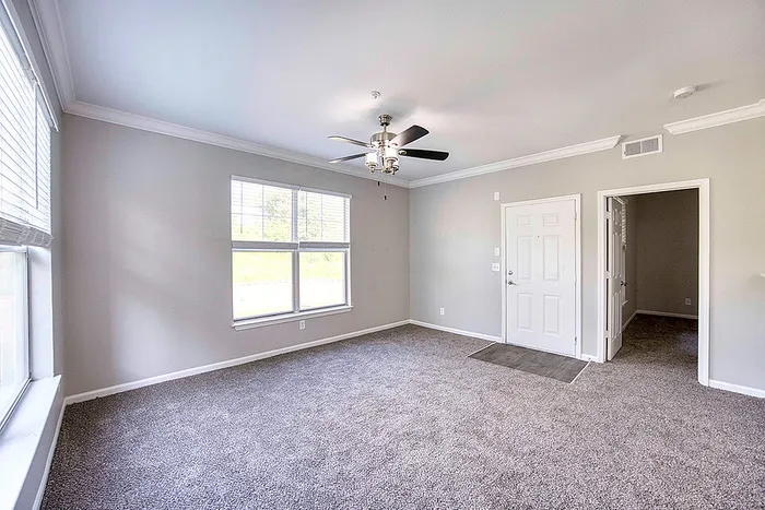 Bright living room with large windows, modern ceiling fan, and plush carpet, offering a cozy and inviting atmosphere.