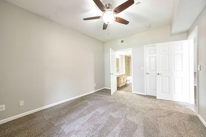 Bright bedroom with plush carpet and ceiling fan, leading to an elegant ensuite bathroom.
