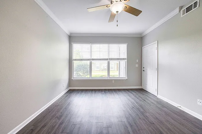 Bright, airy living room featuring modern hardwood flooring, large window with elegant blinds, and a stylish ceiling fan.