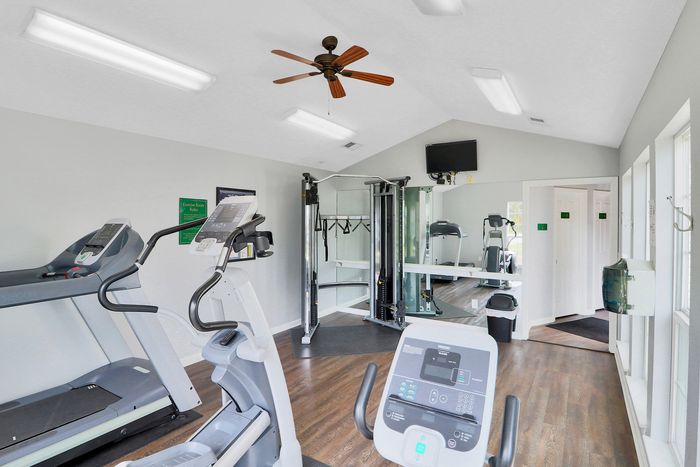 Modern fitness center with state-of-the-art equipment, including treadmills and weight machines, set in a bright room with large windows and stylish wooden flooring.