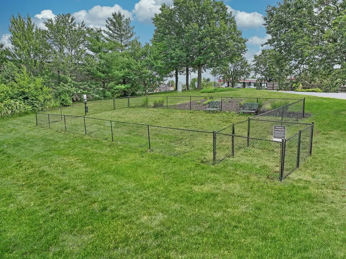 Inviting fenced dog park surrounded by lush greenery and trees, featuring ample space for pets to play and benches for relaxation.