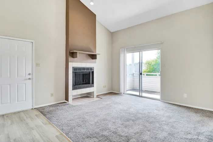 Bright living room with cozy fireplace, plush carpet, and sliding glass door leading to a private balcony with scenic views.