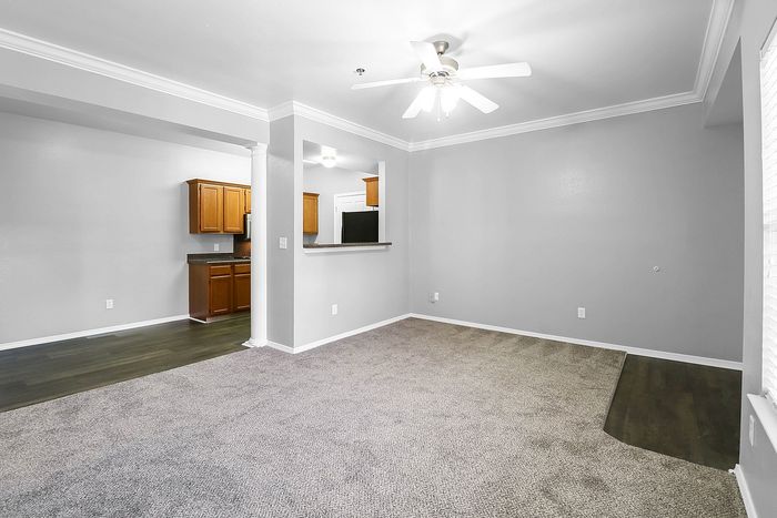 Bright and inviting open-concept living space with modern finishes, featuring plush carpet and a sleek fan. Adjacent kitchen boasts elegant cabinetry for a contemporary touch.