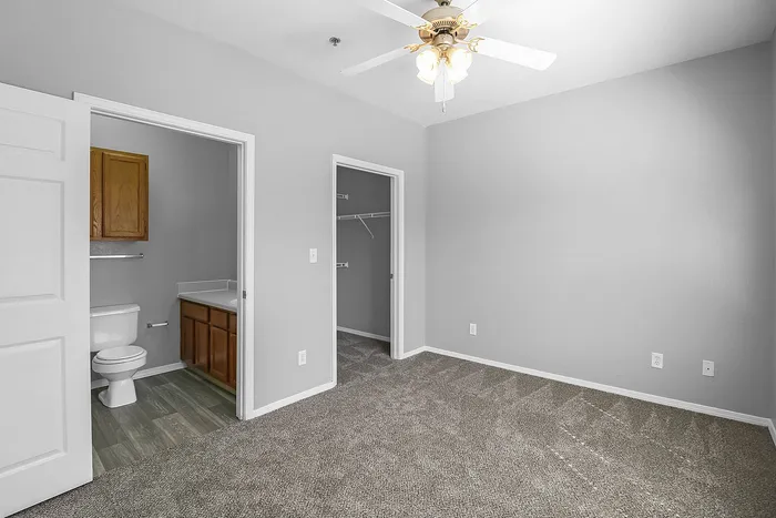 Spacious bedroom featuring plush carpet, ceiling fan, and adjoining en-suite bathroom with modern fixtures.