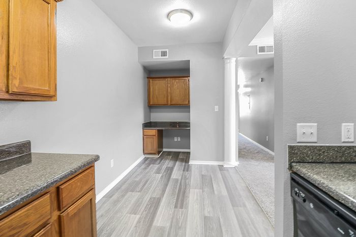 Bright and modern kitchen space with sleek countertops, rich wood cabinetry, and elegant flooring, leading into a cozy hallway.