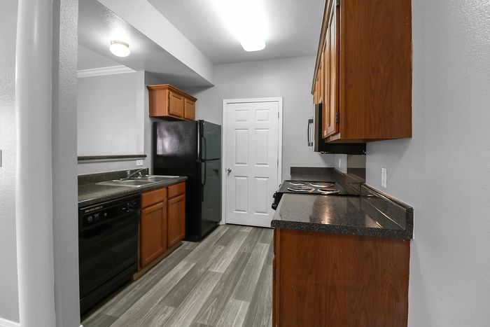 Sleek modern kitchen with dark countertops, warm wood cabinets, and stainless steel appliances in a cozy apartment setting.