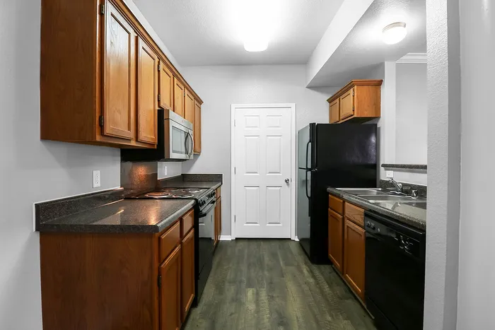 Modern kitchen with sleek black appliances, warm wooden cabinets, and elegant countertops, perfect for culinary creativity.