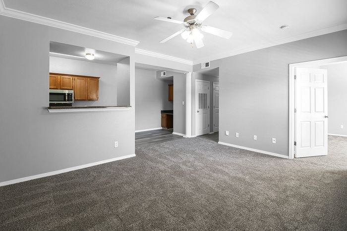 Bright and inviting living space with plush carpeting, ceiling fan, and open kitchen passthrough.