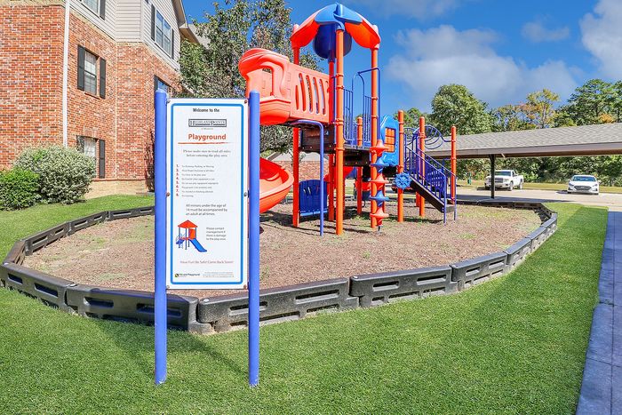 Charming community playground featuring vibrant red and blue play structures in a well-maintained garden setting.