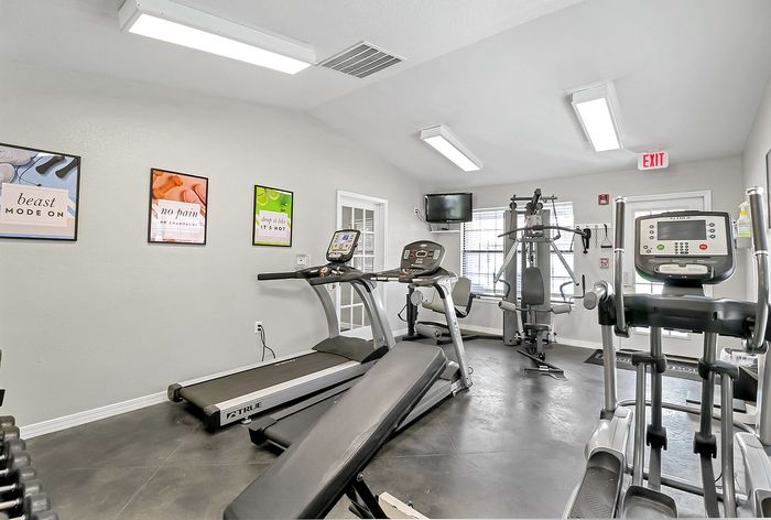 Bright, modern fitness room equipped with treadmills, elliptical, and a multi-station gym machine, featuring motivational posters on the walls.
