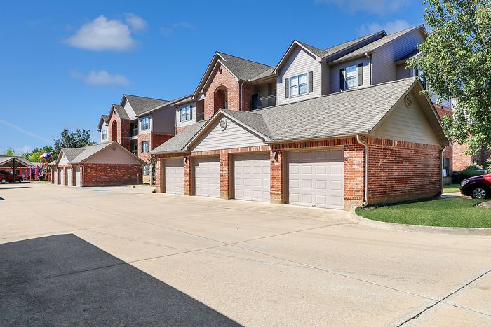Inviting apartment complex featuring modern brick architecture, spacious garages, and a well-maintained community area under a clear blue sky.