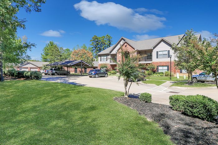 Charming suburban apartment complex with scenic landscape, ample parking, and cozy brick buildings under a clear blue sky.