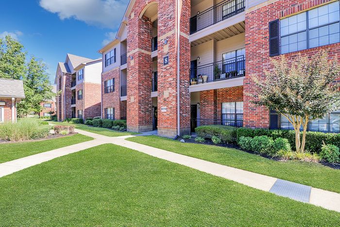 Charming red-brick apartment building with lush green lawns and inviting walkways, perfect for modern living.
