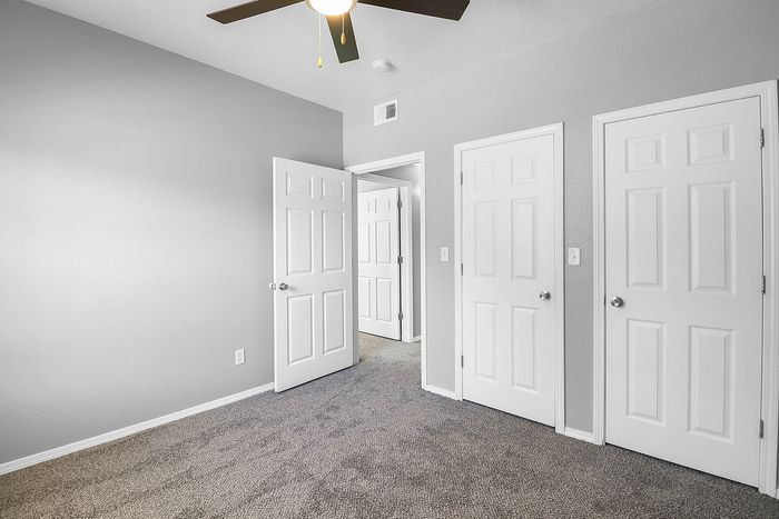 Bright and inviting bedroom featuring plush carpet, modern ceiling fan, and ample closet space with white doors.