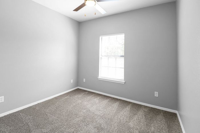 Bright bedroom with soft grey walls, plush carpet, and a ceiling fan, perfect for comfort and relaxation.