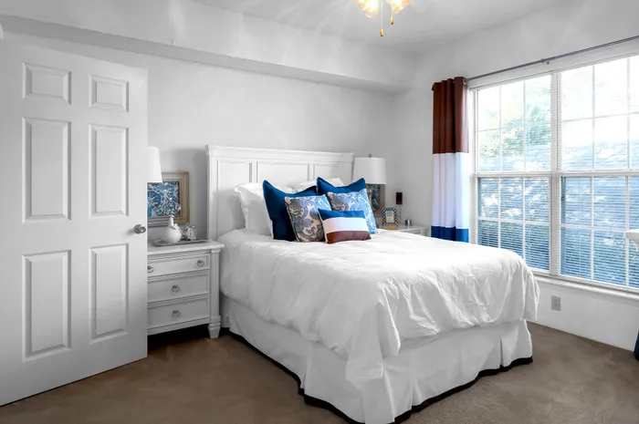 Bright and cozy bedroom with plush bedding, elegant decor, and abundant natural light from large windows, creating a relaxing ambiance.