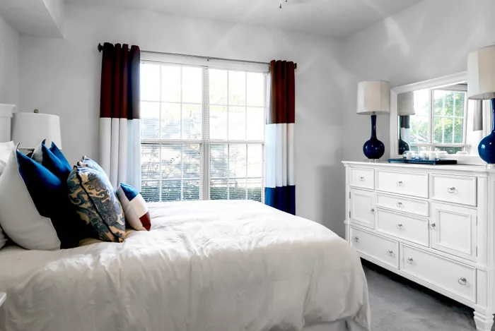 Bright and airy bedroom showcasing a large window, elegant white dresser, and chic decor with blue accents.
