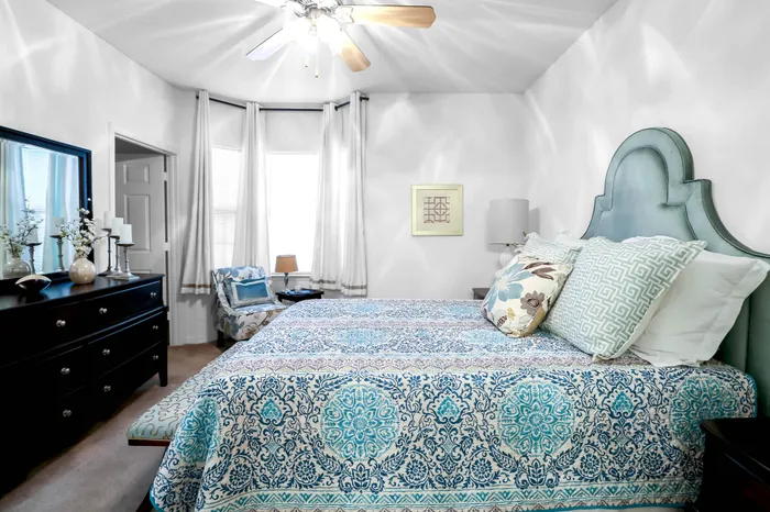 Elegant bedroom featuring a stylish blue patterned bedspread, cozy seating area, and chic contemporary decor, bathed in natural light.