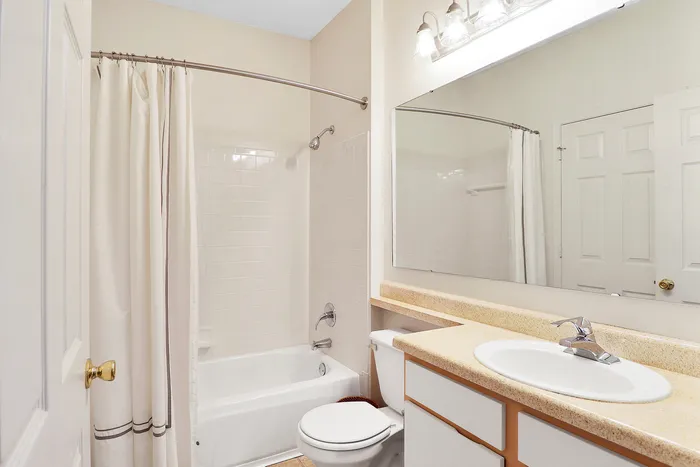 Bright and pristine bathroom featuring a sleek vanity with an elegant countertop, a large mirror, and a cozy bathtub with a soft white curtain.