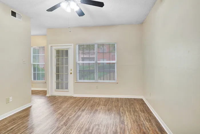 Bright and inviting living area with elegant wood flooring, modern ceiling fan, and large windows for natural light.