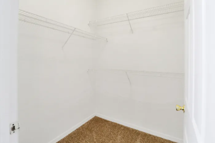 Spacious walk-in closet with white wire shelving and carpeted floor in a modern apartment.
