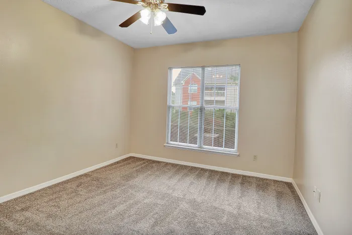 Bright bedroom featuring plush carpet, a large window with natural light, and a modern ceiling fan.